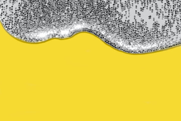 transparent liquid with silver glitter pouring over a pastel yellow background