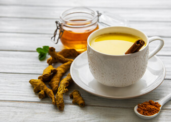 Yellow turmeric latte drink. Golden milk with cinnamon, turmeric, ginger  and honey over white wooden background.