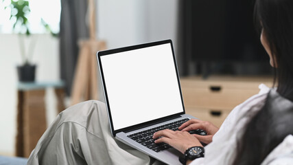 A young female relaxing on sofa and using laptop computer mock up blank white screen.