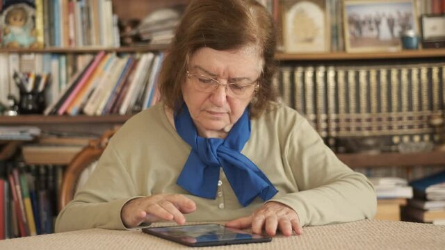 Tablet. Senior adult using digital technology device indoors. Touching screen.