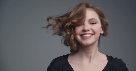 Young happy girl shaking her hair. Slow motion footage of an  attractive brown-haired woman. Cheerful model moves her head to the sides. Beautiful woman with medium long curly brown hair.