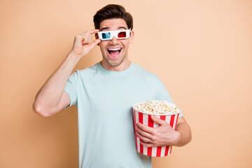 Portrait of nice cheerful amazed guy eating pop corn watching film touching 3d specs isolated over beige pastel color background