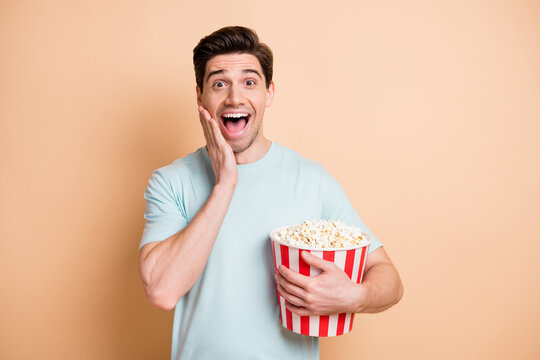 Portrait of nice cheerful guy eating pop corn watching funny film having fun isolated over beige pastel color background