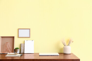 Stylish workplace with blank photo frame near color wall