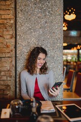 Copy space in close-up smiling woman portrait. Attractive young caucasian lady sitting in a table restaurant using smartphone. Electronic devices, technology, communication concept.