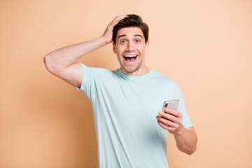 Portrait of nice cheerful amazed guy influenzer using device browsing media news smm isolated over beige pastel color background