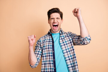 Portrait of attractive cheerful crazy guy wearing checked shirt rejoicing isolated over beige pastel color background