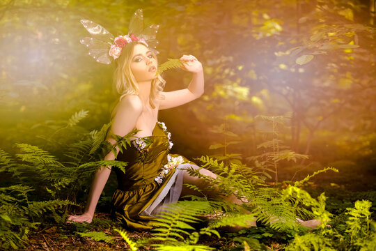 Portrait of Cute Sensual Caucasian Female Posing With Decorative Butterfly Garland and Green Flowery Dress In Forest with Added Light Flares.