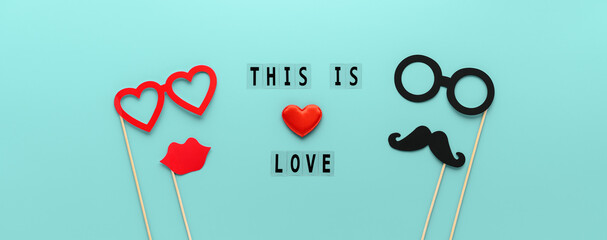 Lettering This is Love and paper props mustache, lips and glasses on pastel turquoise background. Concept Valentine's Day and love. Creative flat lay, wide banner © Ramil Gibadullin
