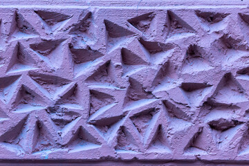 The corrugated surface of a plastered concrete wall covered with triangular depressions and recesses.