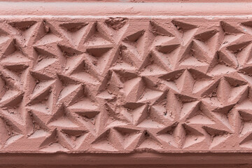 The corrugated surface of a plastered concrete wall covered with triangular depressions and recesses.