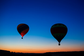 Fototapeta premium Two Colorful Air Balloons Levitating Over the Field Outdoors Against Clear Blue Skies At Twilight.