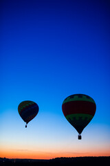Two Colorful Air Balloons Levitating Over the Field Outdoors Against Clear Blue Skies At Twilight.