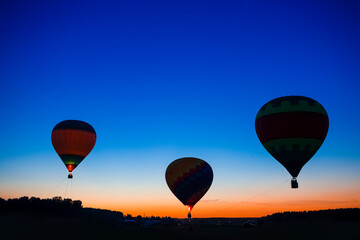Three Amazing Colorful Air Balloons Levitating Over the Ground Outdoors Against Clear Blue Skies At Twilight.