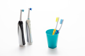 Professional Electric Toothbrushes In Front of Two Manual Tooth Brushes in One Cup On White