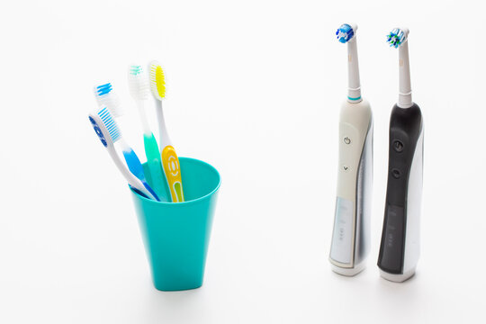 Professional Electric Toothbrushes In Front of Four Manual Tooth Brushes in One Cup On White Background.