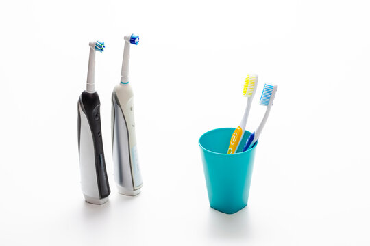 Professional Electric Toothbrushes In Front of Two Manual Tooth Brushes in One Cup On White