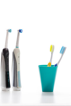 Professional Electric Toothbrushes In Front of Two Manual Tooth Brushes in One Cup On White Background.