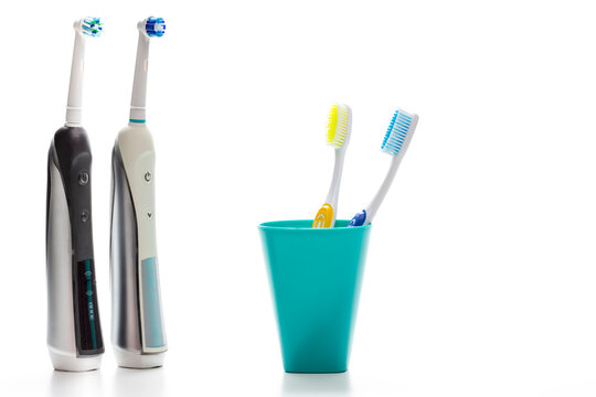Pair of Professional Electric Toothbrushes In Front of Two Manual Tooth Brushes in One Cup On White