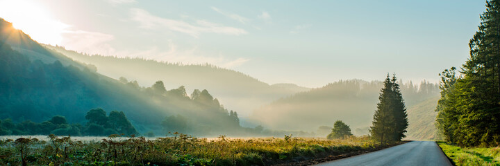 panorama of mountains in the fog near the road at sunrise. beautiful background