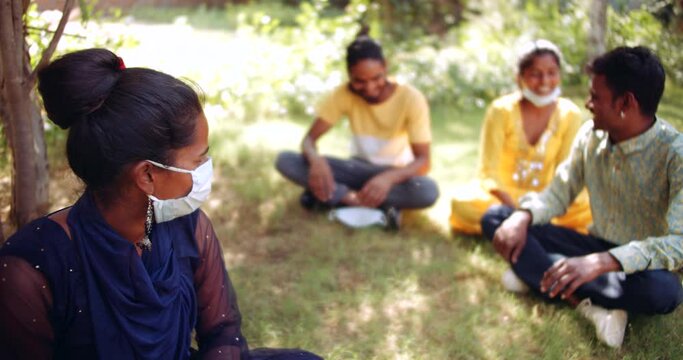 Slow-motion Static Medium-shot MS Of One Female Friend In The Nature Park Garden As She Wears Her Face Mask Pulls It Up Talks To Her Friends While She Is Maintaining Social And Physical Distance