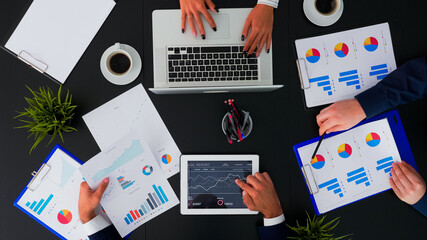 Top view of office workers discussing business financial diagrams and working on digital devices. Working in team conference with project planning document and modern technology on company table.