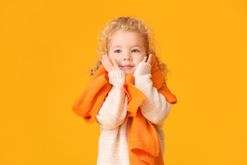 Cute little girl with warm scarf on color background