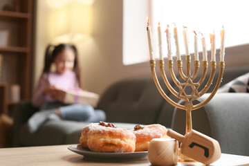 Menorah, dreidels and donuts on table of happy little girl celebrating Hannukah at home