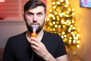 a man takes a breath through a lung inhaler in front of Christmas lights