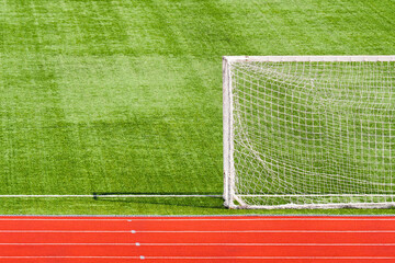 Empty green sport field with football goal and red running tracks, open stadium