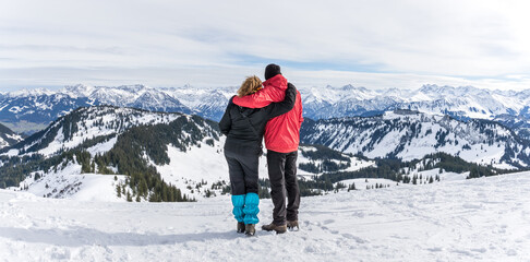 Senior couple is hiking in alpine snow winter mountains enjoying panorama view. Allgau, Bavaria, Germany.
