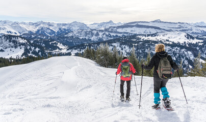 Fototapeta na wymiar Senior couple is snowshoe hiking in alpine snow winter mountains. Allgau, Bavaria, Germany.