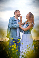 Young beautiful couple having fun on natural background. Date of guy and girl on a green field with glass and flowers in cloudy summer day. Yound family having rest together