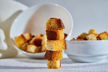 Square toasted pieces of homemade delicious rusk, hardtack, Dryasdust, zwieback stand in columns near white plate on a white tablecloth.
