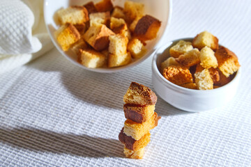Square toasted pieces of homemade delicious rusk, hardtack, Dryasdust, zwieback stand in columns near white plate on a white tablecloth.