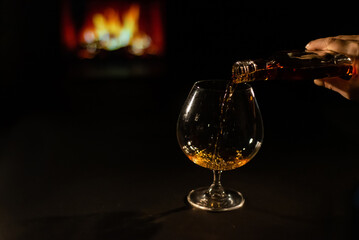 Close-up of a female hand with a glass of brandy on the background of the fireplace