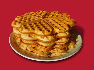 Typical German waffles in the shape of a heart. They are baked in a waffle iron. Five pieces are on a plate. Isolated with red background.