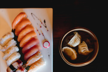 Top view Japanese food on settled up restaurant table.
Plate with mix of Nigiri sushi and  steamed dumplings.
