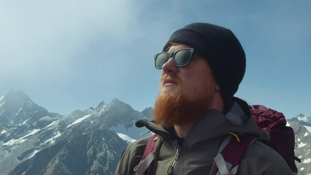 Portrait of a man with a beard and glasses of Scandinavian appearance on the background of high rocky mountains with snow 4k