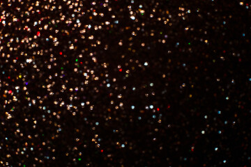 Sparkling background from small sequins, closeup of particles color of light on a black background