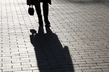 Silhouette of woman with bag walking down the street, black shadow on pavement. Female legs on sidewalk, concept of dramatic life story