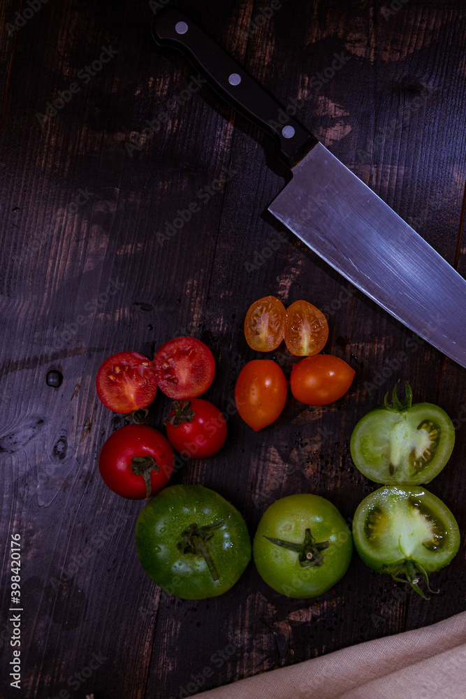 Sticker Vertical shot of sliced ripe and unripe tomatoes with knife and napkin on a wooden table