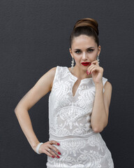 A girl model in a wedding dress with jewelry earrings and a fashionable hairstyle poses on a gray background. Modern bride wirk professional makeup
