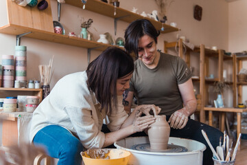 Loving couple dating in pottery workshop, man and woman sit at the pottery wheel and modeling clay