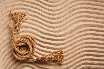 Fototapeta na wymiar Sturdy marine rope on wavy texture sand. A place for text or for an advertising product. Top view.
