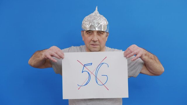 Frightened man in a tinfoil hat waved off the 5G waves.5G tower radiation protection. Irrational fear of a non-existent problem. Protective foil helmet to the brain from aliens.