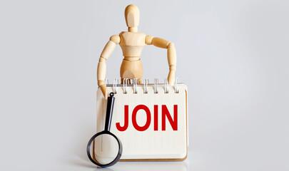 Wooden man shows with a hand to white notepad with text JOIN