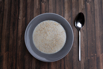 A plate of porridge with a spoon on a wooden table, top view and copy space