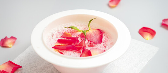 A white bowl of water with pink rose petals on a white table in the spa salon
