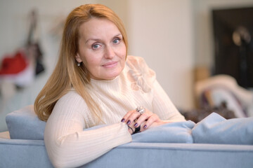 Smiling happy woman at home. Smiling middle-aged blond woman with a beaming smile sitting on a sofa at home looking at the camera